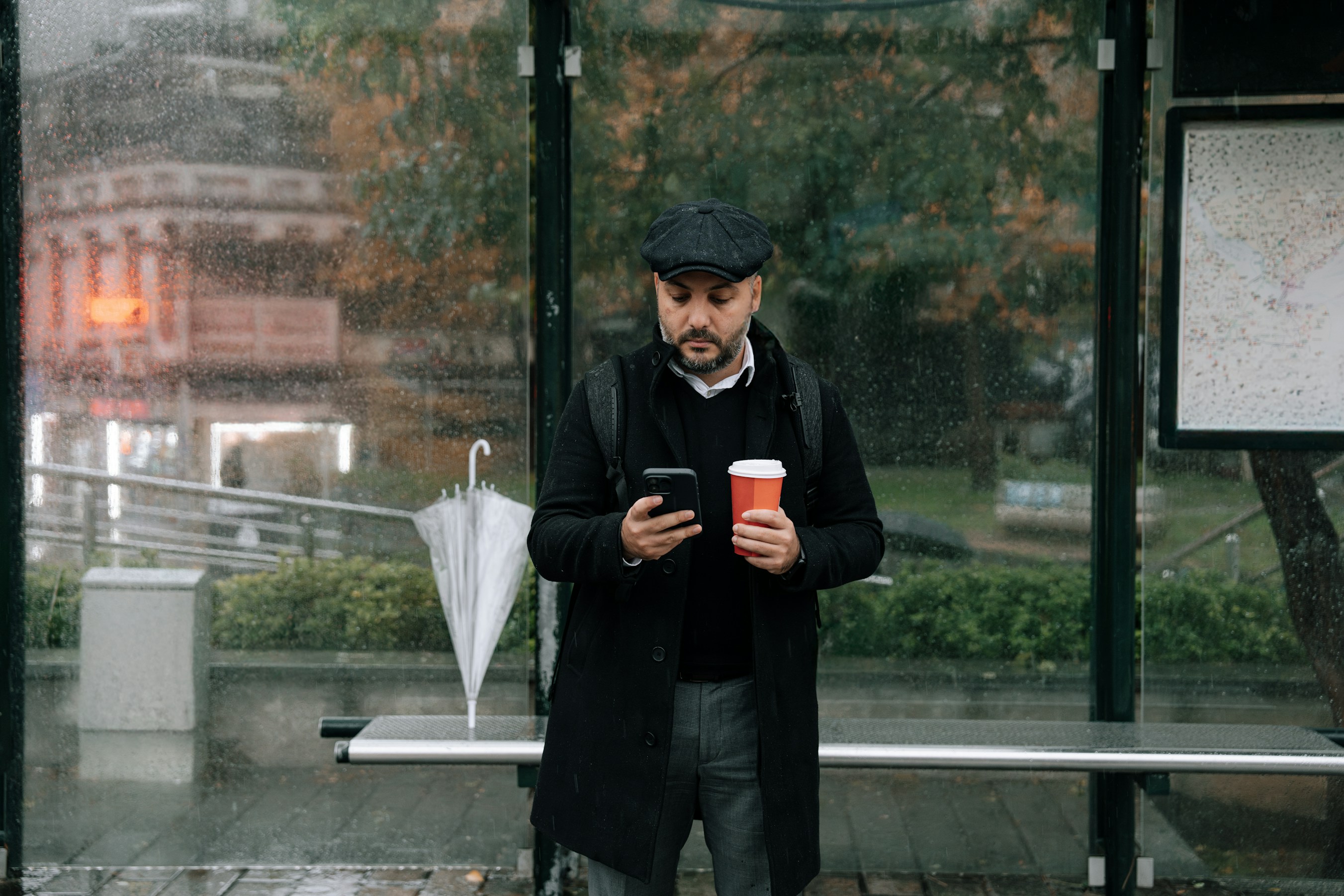 Een man kijkt op zijn telefoon bij de bushalte